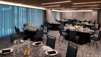 The image shows a modern, elegantly set banquet hall with round tables dressed in black tablecloths, set with dishes and glasses, and decorated with floral centerpieces.