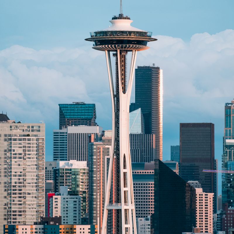 The image shows the Space Needle in Seattle, surrounded by various skyscrapers and buildings, under a cloudy sky.