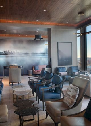 A modern lounge with comfortable seating, a cityscape mural, large windows offering scenic views of water and a Ferris wheel in the distance.