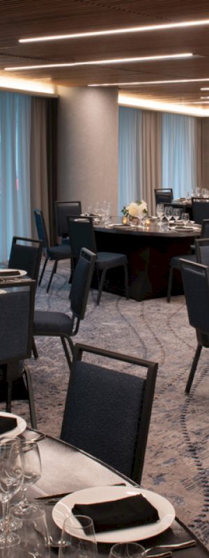 The image shows an elegantly set dining room with round tables arranged for an event. The tables are decorated with black napkins and white flowers.