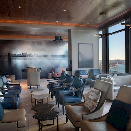 The image shows a modern lounge area with stylish chairs, a large window with a scenic view, and contemporary decor, likely in a high-rise building.