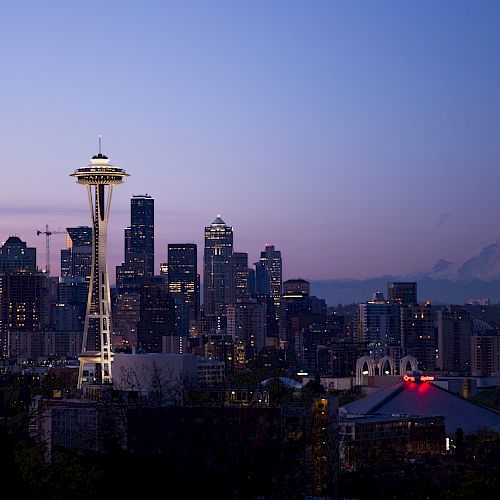 The image shows the Seattle skyline at dusk, featuring the Space Needle prominently with Mount Rainier visible in the background.