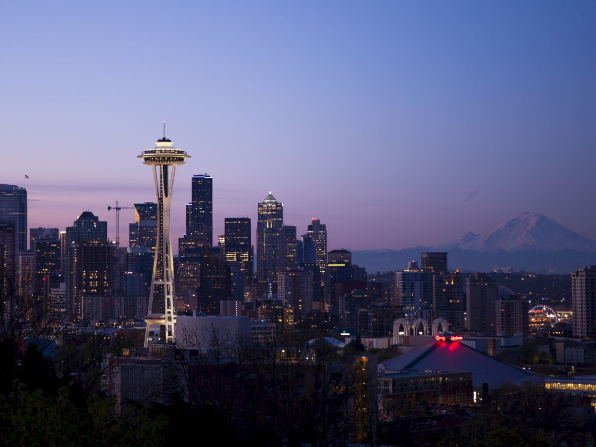 This image shows a cityscape at dusk with the iconic Space Needle and downtown Seattle buildings, plus Mount Rainier in the background.