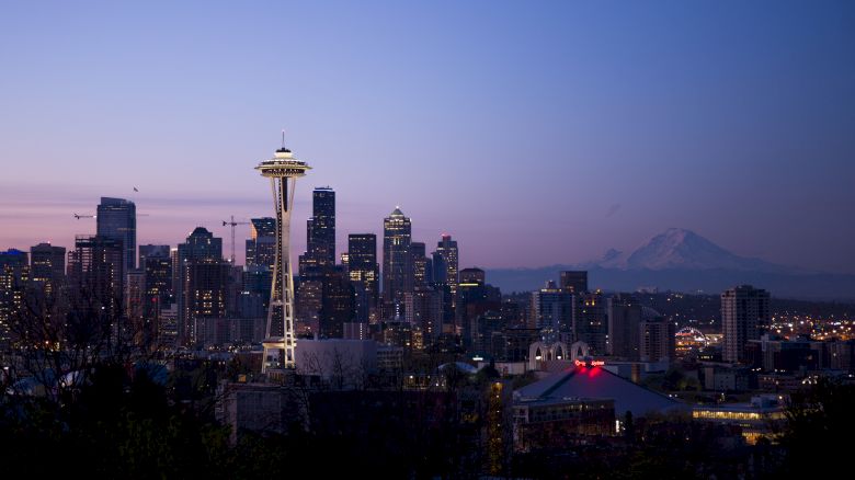 This image shows a cityscape at dusk with the iconic Space Needle and downtown Seattle buildings, plus Mount Rainier in the background.